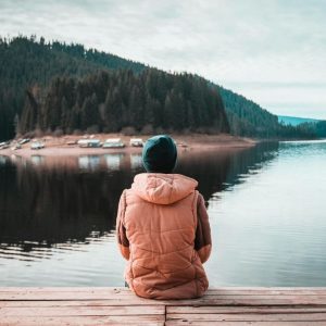 Person sitting on wooden dock overlooking calm mountain lake.